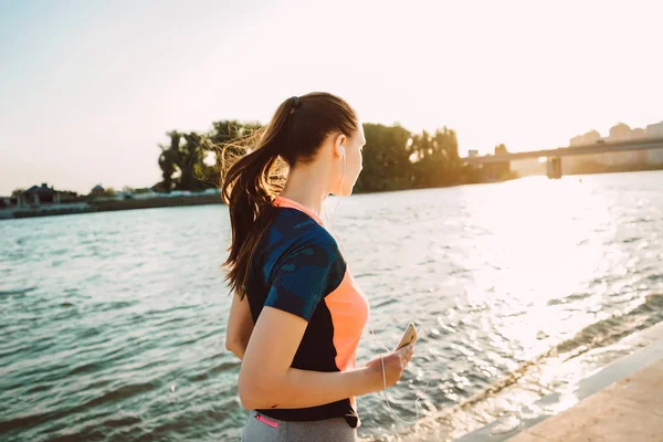 En sport-tjej med en telefon i hennes händer utför en kväll kör — Stockfoto