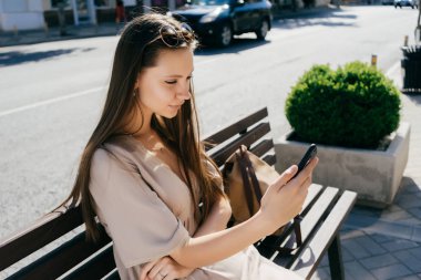 selfie smartphone cep telefonu ile yapıyorsun, tahta bankta oturan bej elbiseli çekici genç kız
