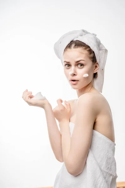 Verrast meisje in een witte handdoek op hoofd reiniging schuim toe te passen op gezicht — Stockfoto