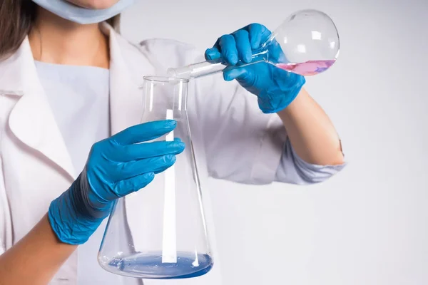 Ragazza farmacista in abito protettivo bianco e guanti di silicone blu mescola preparazioni chimiche in fiaschette — Foto Stock