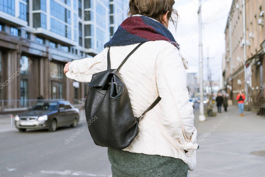 stylish young girl walks, in a light jacket and with a black backpack