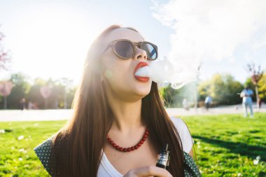 Mutlu moda gülümseyen kadın güneş gözlüğü vape Street, duman Sigara
