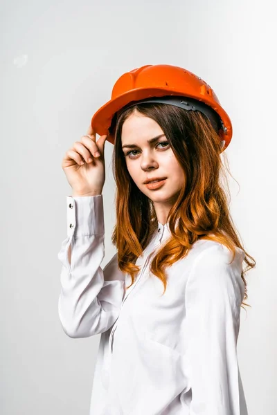 Uma menina em uma camisa branca e um capacete de construção laranja olha em frente . — Fotografia de Stock