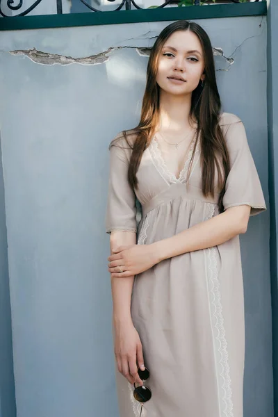 Uma menina em um vestido de verão cinza posando contra uma parede cinza — Fotografia de Stock