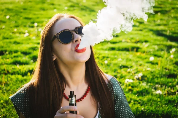 Glada mode leende kvinna i solglasögon rökning vape på street, rök — Stockfoto