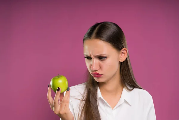 Fehér ing-elégedetlen fiatal lány zöld alma tart a kezében, és néz rá — Stock Fotó