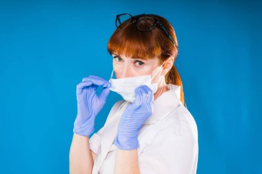 gözlük ve yüz maskesi kameraya bakarak giyiyor yetişkin zeki Kızıl saçlı kadın doktor