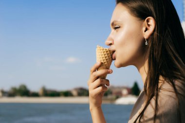 sevimli genç kız nehir ve gökyüzünde güneşin arka planı dondurma yiyor