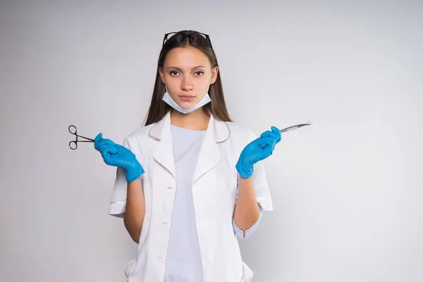 Grave giovane medico ragazza in vestaglia medica bianca e guanti blu tiene strumenti medici in mano — Foto Stock