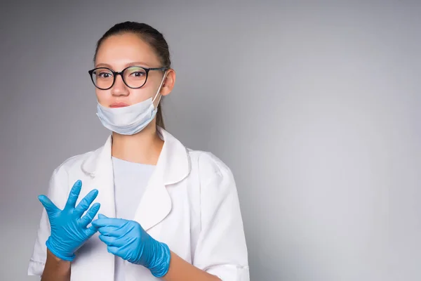 Ung självsäker tjej läkaren i glasögon och ansikte mask tar bort handskar från händerna — Stockfoto