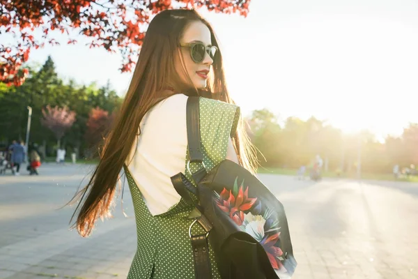Mujer de moda en gafas de estilo callejero con bolsa, puesta de sol — Foto de Stock