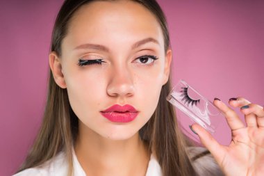 Genç kız pembe bir arka plan üzerinde sahte kirpik dayatır
