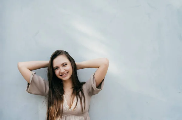 Chica joven en un vestido de verano se apoya contra una pared gris — Foto de Stock