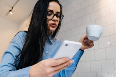 başarılı genç iş kadını bardaklarda bir kafede çalışıyor, kahve içer, bir akıllı telefon elinde tutan ve görünüyor