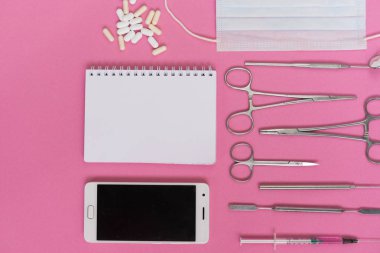 bir akıllı telefon, bir dizüstü bilgisayar, hap ve tıp aletleri, bir şırınga ve bir yüz maskesi pembe bir arka plan olduğunu