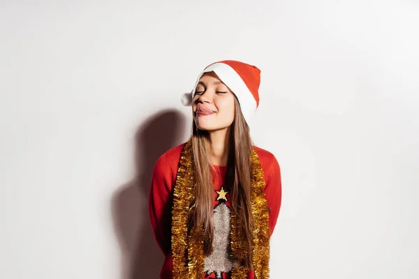 Engraçada menina feliz celebra o ano novo e Natal, mostra a língua, sorrisos, em boné vermelho como santa claus — Fotografia de Stock
