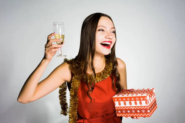Забавная красивая молодая девушка празднует Новый год и Рождество, пьет шампанское из бокала, получила подарок — стоковое фото