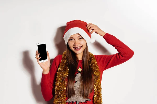Lustiges Mädchen wartet auf Neujahr und Weihnachten, sieht glücklich aus, lacht, zeigt ihr Smartphone — Stockfoto
