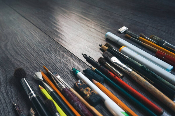 на темном деревянном полу художественные аксессуары кисти, карандаши, перья
