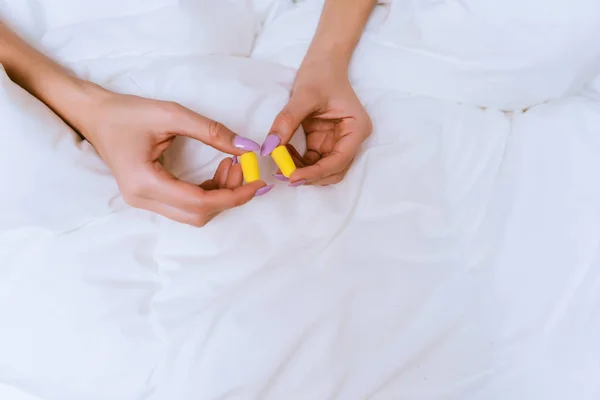 Het meisje zit in een witte bed en houdt de gele oordoppen — Stockfoto