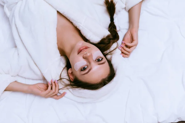 Ein junges Mädchen liegt in einem weißen Mantel im Bett, gerade aufgewacht, unter den Augen von Silikonflecken gegen blaue Flecken — Stockfoto