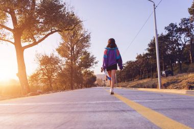 bir kaykay elinde tutan yol boyunca yürüyüş mor ceket şık genç kız