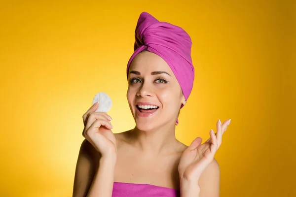 Rolig ung hud med en rosa handduk på huvudet rengör ansiktet med en bomullspad, leende — Stockfoto