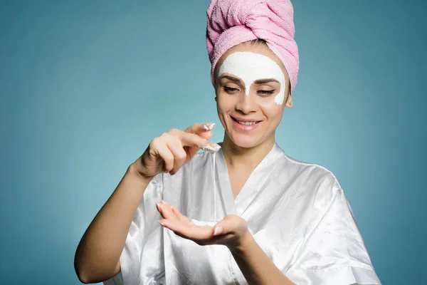 Happy νεαρό κορίτσι με μια ροζ πετσέτα στο κεφάλι της, εφαρμόζοντας μια θρεπτική μάσκα στο πρόσωπό της — Φωτογραφία Αρχείου