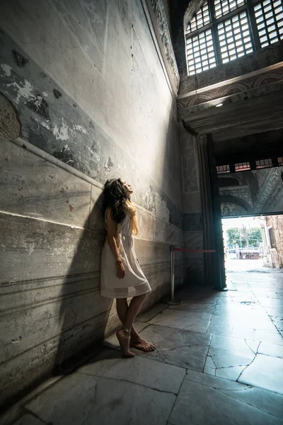 Believer girl stands in the temple in the rays of light and looks up in search of God