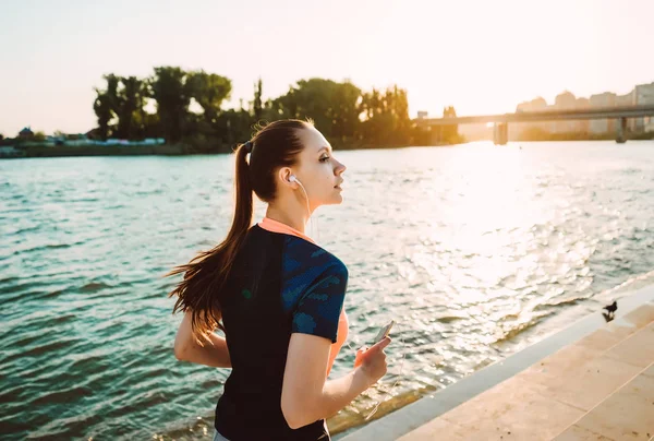 En flicka i en sportig enhetlig går längs floden vid solnedgången — Stockfoto