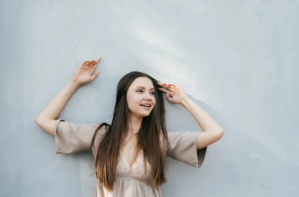 Молодая девушка в летнем платье позирует против серой стены улыбаясь — стоковое фото