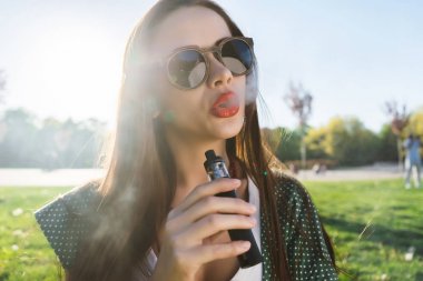 Mutlu moda gülümseyen kadın güneş gözlüğü vape Street, duman Sigara