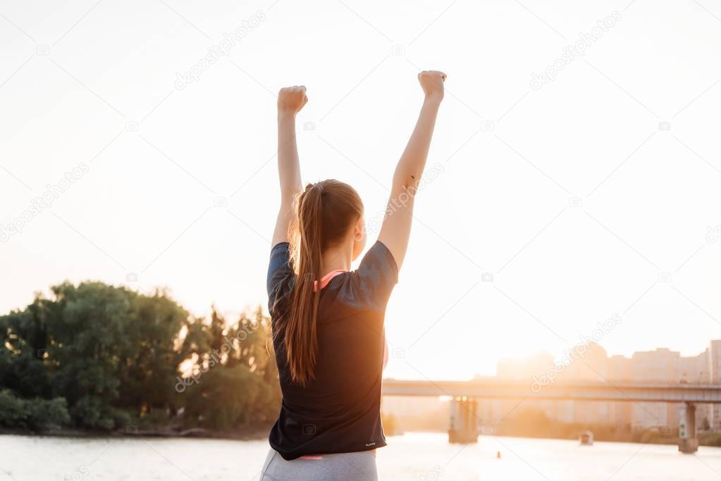 a girl in a tracksuit on a run on the river bank. Woman doing exercises and raising her hands up