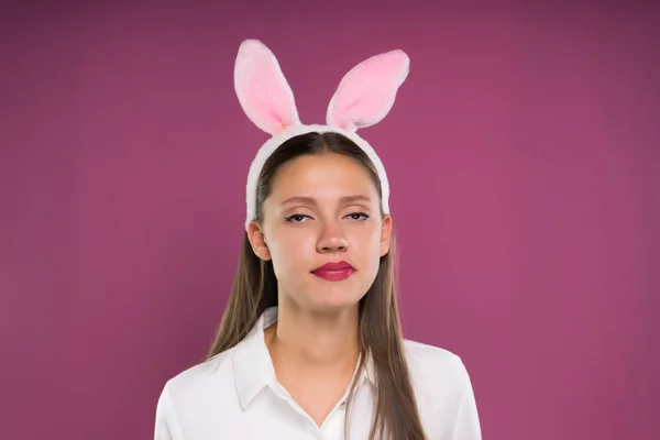 Bella ragazza con le orecchie di lepre rosa sulla testa guardando scontento la fotocamera e mastica — Foto Stock