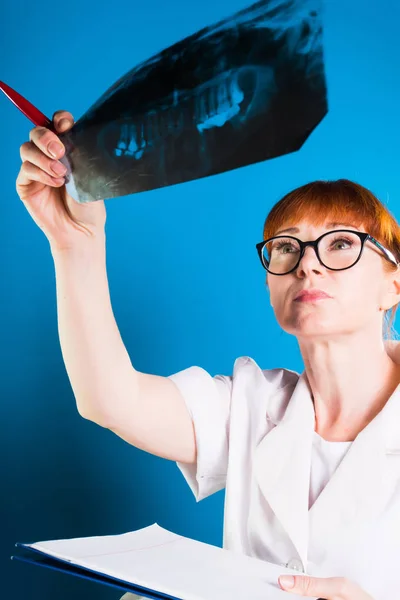 Rothaarige Krankenschwester mit Brille schaut sich das Röntgenbild an und schreibt dem Tagebuch, isoliert — Stockfoto