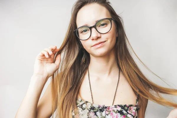 Menina positiva, bonito menina de cabelos longos com óculos está segurando seu cabelo e sorrindo para a câmera — Fotografia de Stock