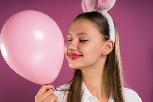 一个女孩用野兔的耳朵捧着一个粉红色的球在她的手, 看着他的可爱 — 图库照片