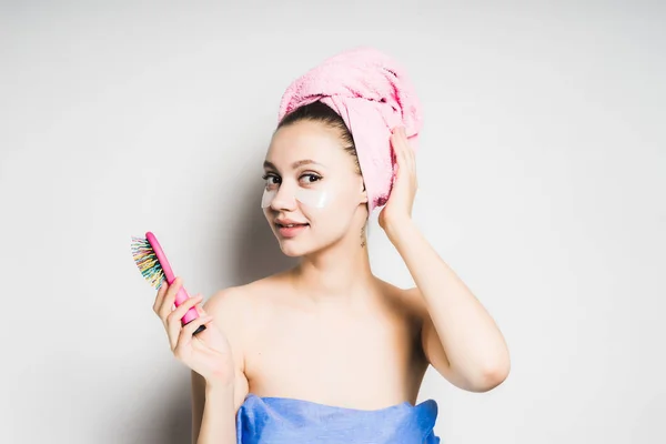Fröhliches Mädchen nach der Dusche mit rosa Handtuch auf dem Kopf hält einen Kamm in den Händen und blickt isoliert in die Kamera — Stockfoto