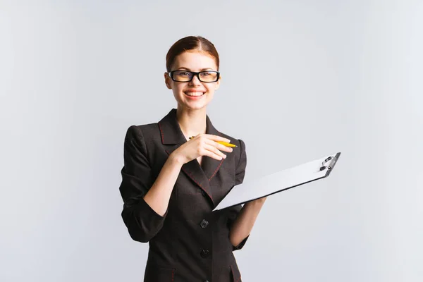 Schönes Mädchen in schwarzem Anzug und Brille, einen Ordner mit Papieren in der Hand haltend und in die Kamera lachend, isoliert — Stockfoto