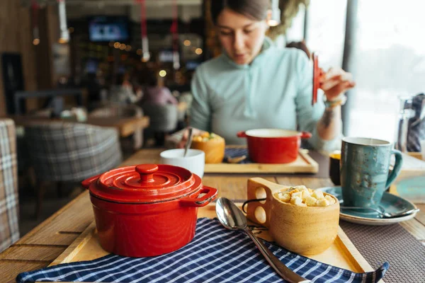 La chica está desayunando en el café después de un paseo, comiendo en una cacerola roja —  Fotos de Stock