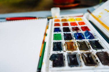 Sanatçının aksesuarlar, renkli suluboya, fırçalar ve kalem masaya vardır