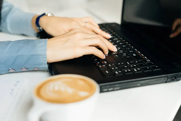 Freelancer menina trabalhando atrás do laptop no café, ao lado da caneca com café — Fotografia de Stock