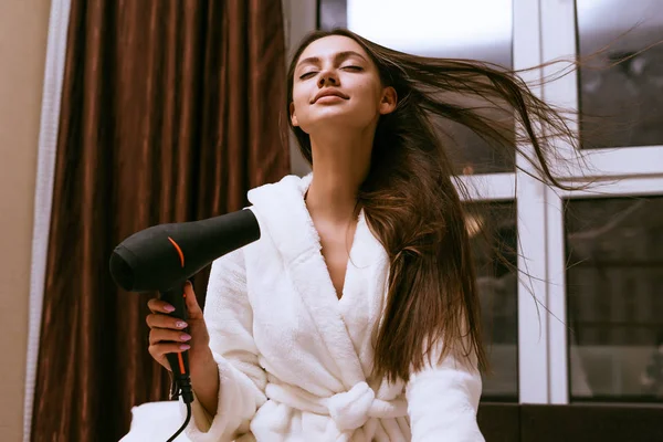 Jovem feliz seca seu longo cabelo grosso com um secador de cabelo preto — Fotografia de Stock