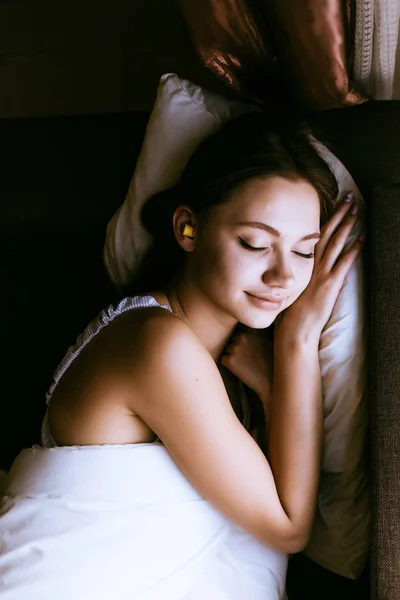 Roztomilá mladá dívka spí u okna, v uších špunty do uší proti hluku — Stock fotografie