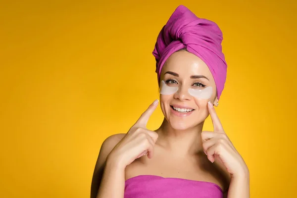 Giovane ragazza felice con un asciugamano rosa sulla testa, sotto gli occhi di macchie di silicone contro lividi — Foto Stock
