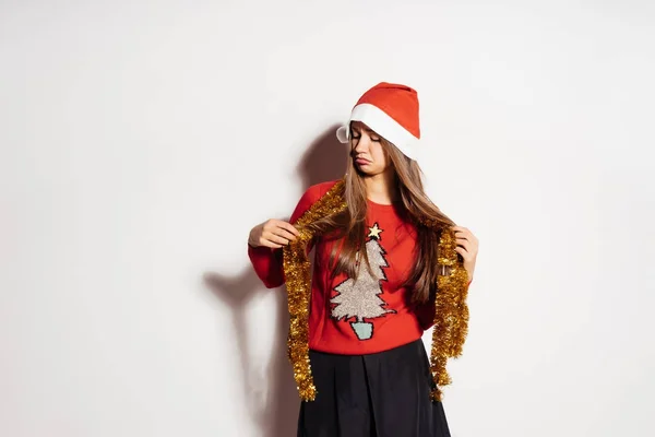 Menina triste em um chapéu festivo esperando o ano novo e Natal, mantém o ouropel de ouro — Fotografia de Stock