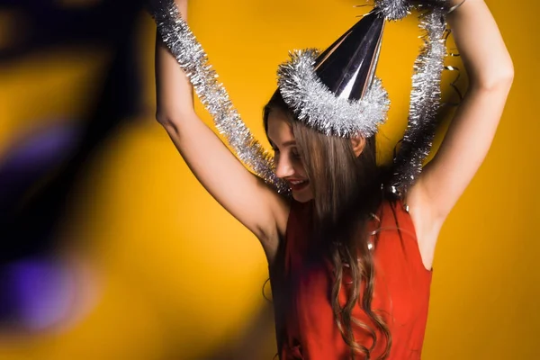 Menina feliz celebra o ano novo e Natal em um gorro festivo, mantém um ouropel de prata — Fotografia de Stock