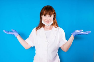 Kızıl saçlı hemşire şirin kameraya bakar ve kollarını mavi bir arka plan üzerinde izole yanlara silah