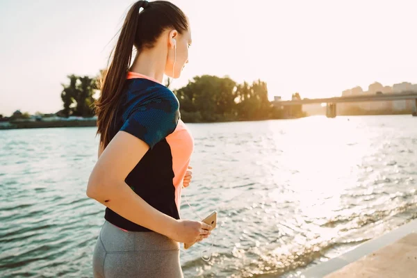 Dziewczyna w garniturze sport jogging na nabrzeżu, słuchanie muzyki na słuchawkach — Zdjęcie stockowe