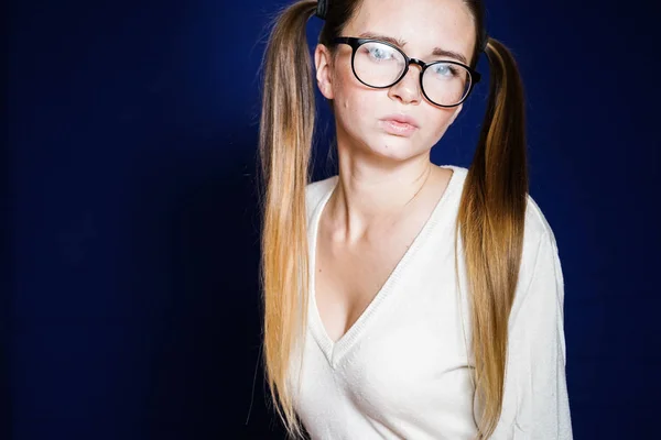 Chica seria con el pelo largo y gafas mira a la cámara, aislado sobre un fondo azul —  Fotos de Stock